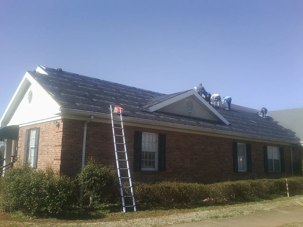 Crew tearing shingles off a brick ranch roof with a ladder set — Metal Roof Repair work by our crew in Hanover