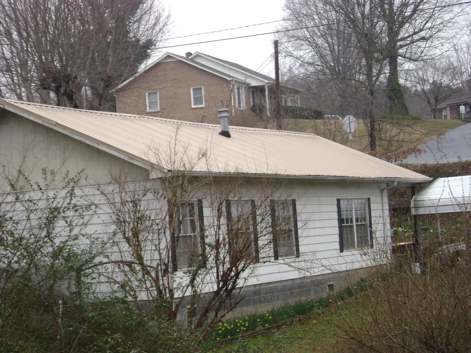 Tan metal roof on a white sided house set into a hillside — Commercial Roofing by Roofing Brothers in Hanover